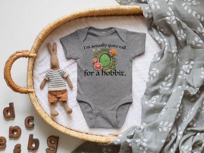 A baby onesie with a humorous text printed on it, placed on a woven basket, alongside a stuffed rabbit and a blanket with a leaf pattern.