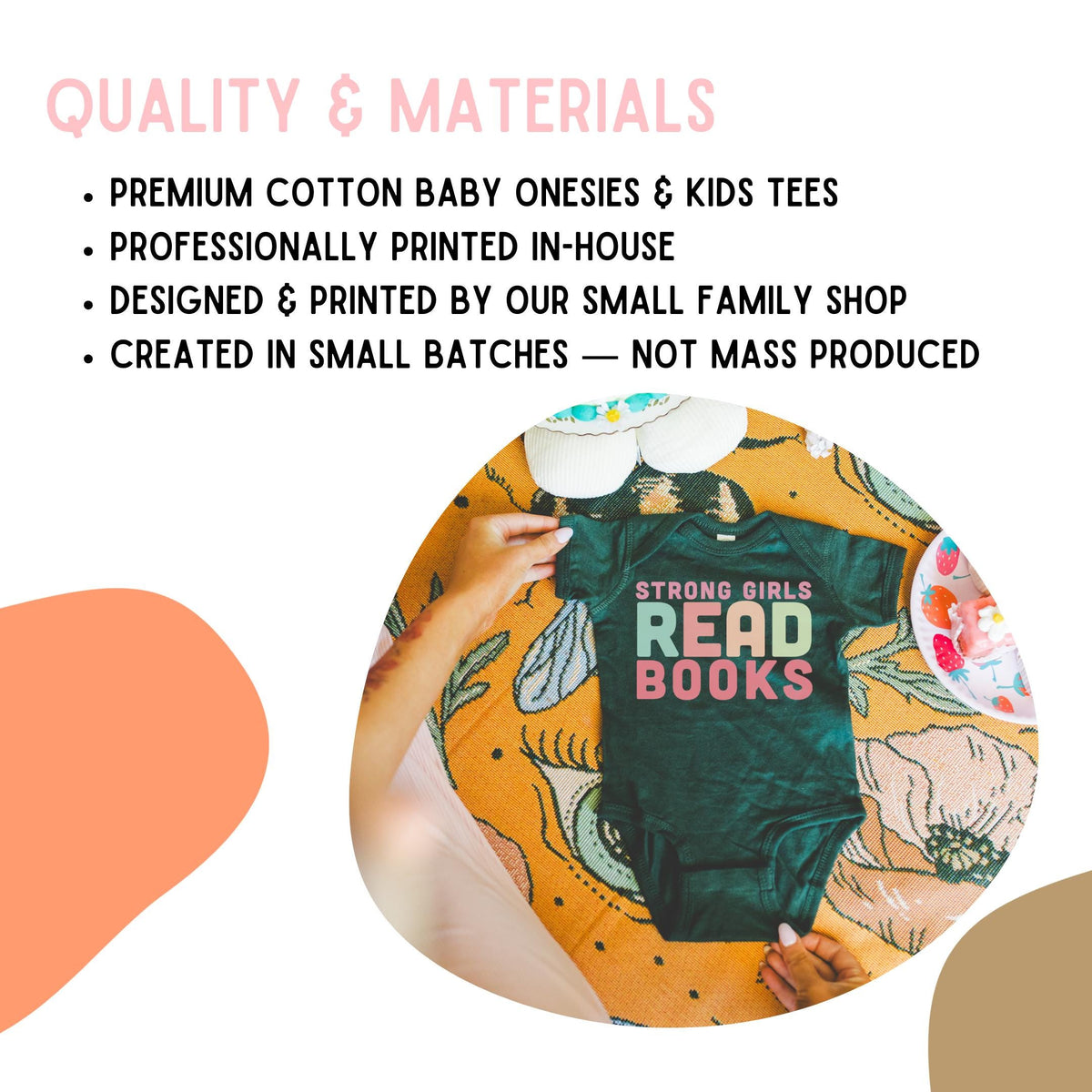 a person's hands holding a baby onesie with the text "STRONG GIRLS READ BOOKS" printed on it, placed on a floral patterned blanket.