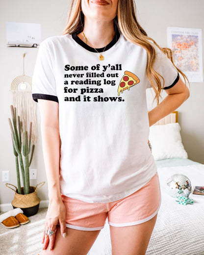 A woman wearing a white t-shirt with a humorous text printed on it, standing in a room with a bed, plants, and a mirror.