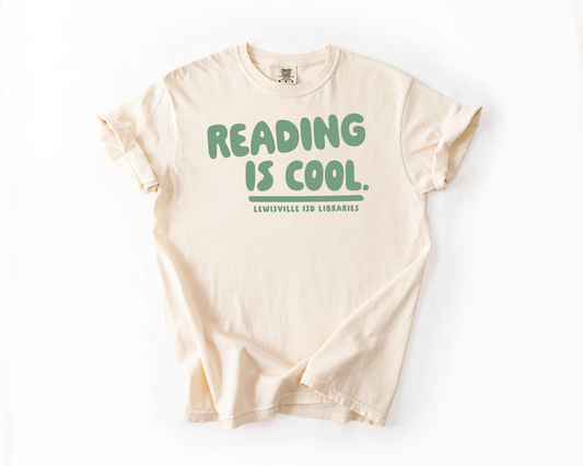 A cream-colored t-shirt with the text "READING IS COOL. LEWISVILLE ISD LIBRARIES" printed on it.