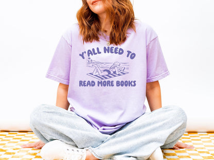 A woman wearing a purple t-shirt with the text "Y'ALL NEED TO READ MORE BOOKS" is sitting cross-legged on a checkered surface.