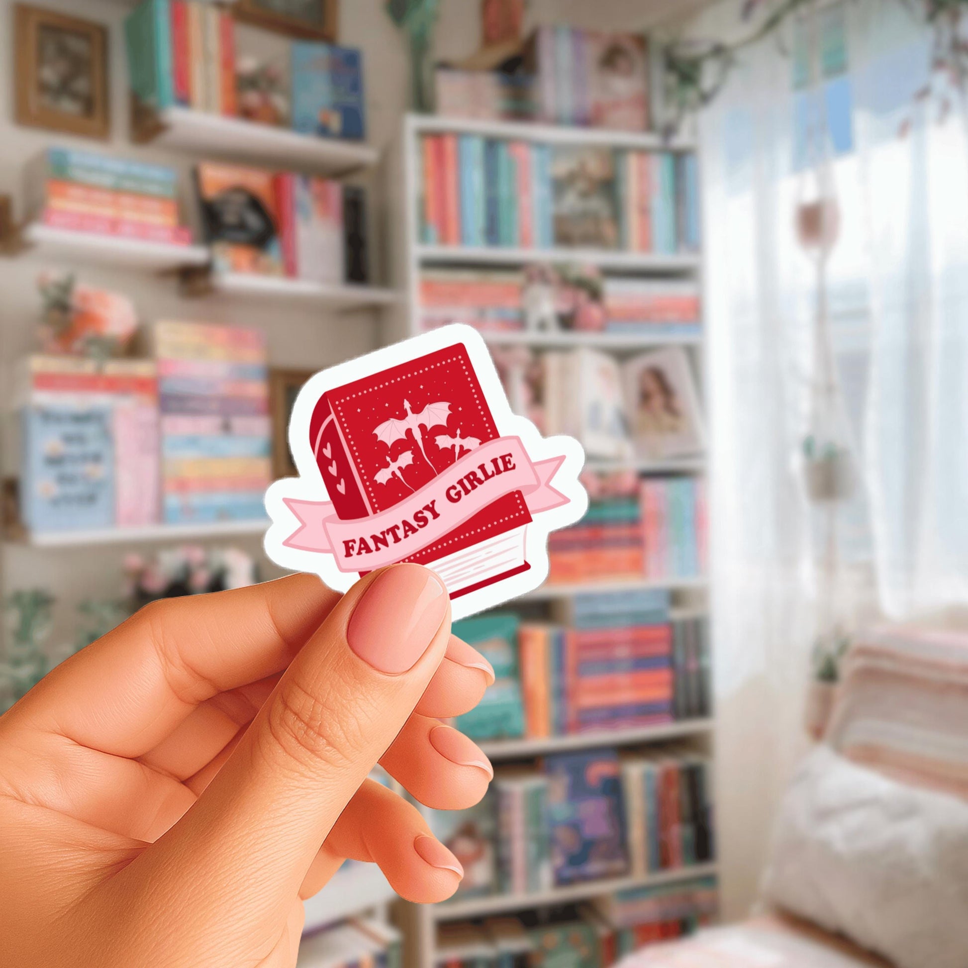 A hand holding a red sticker with the text "FANTASY GIRL" on it, in front of a bookshelf filled with various books.