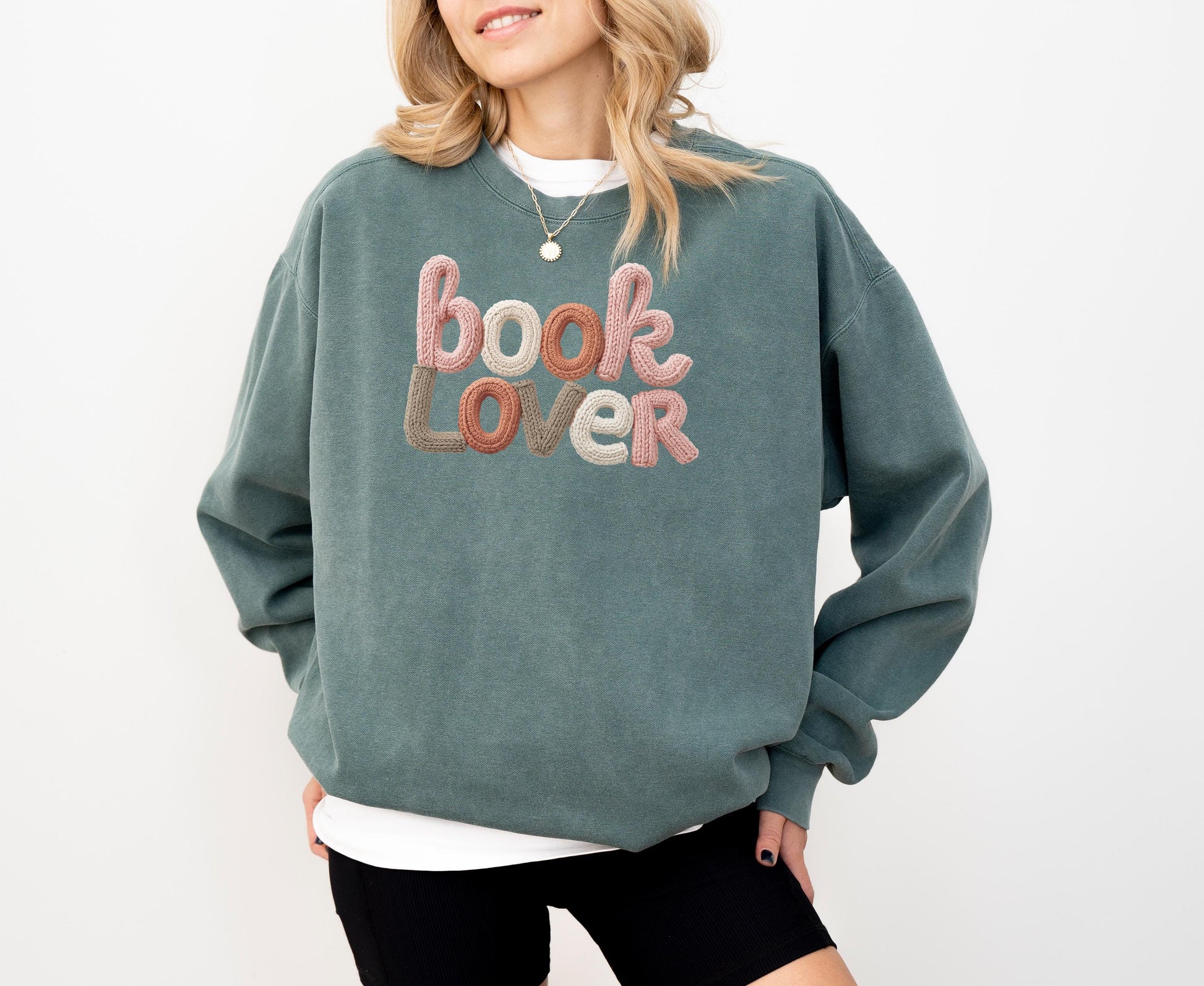 A woman wearing a green sweatshirt with the text "Book Lover" embroidered on it.