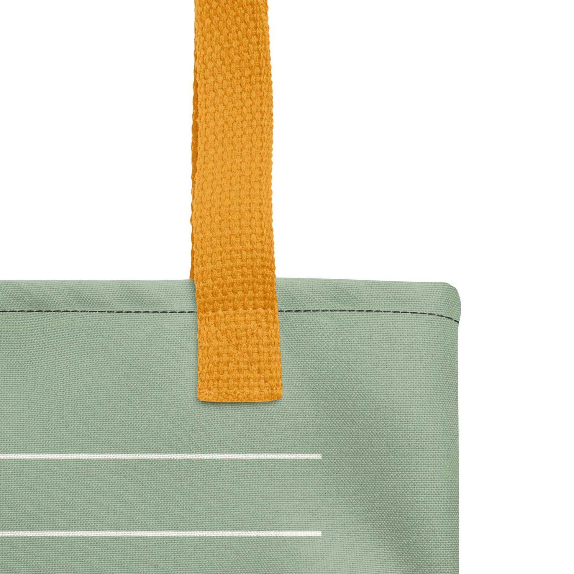 A close-up view of a green fabric bag with a yellow handle, showing the handle and a white line on the fabric.