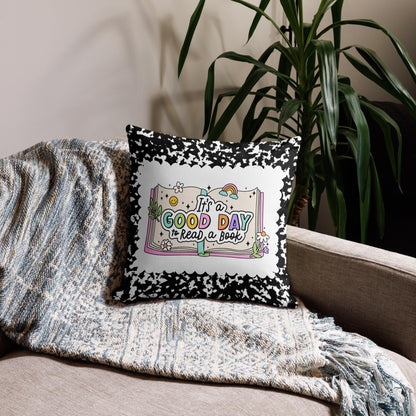 A black and white throw pillow with a colorful graphic design sits on a couch, with a gray blanket and a potted plant in the background.