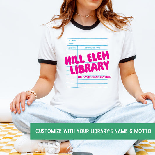 A woman wearing a white t-shirt with a graphic design of a library book and the text "HILL ELEM LIBRARY" printed on it.