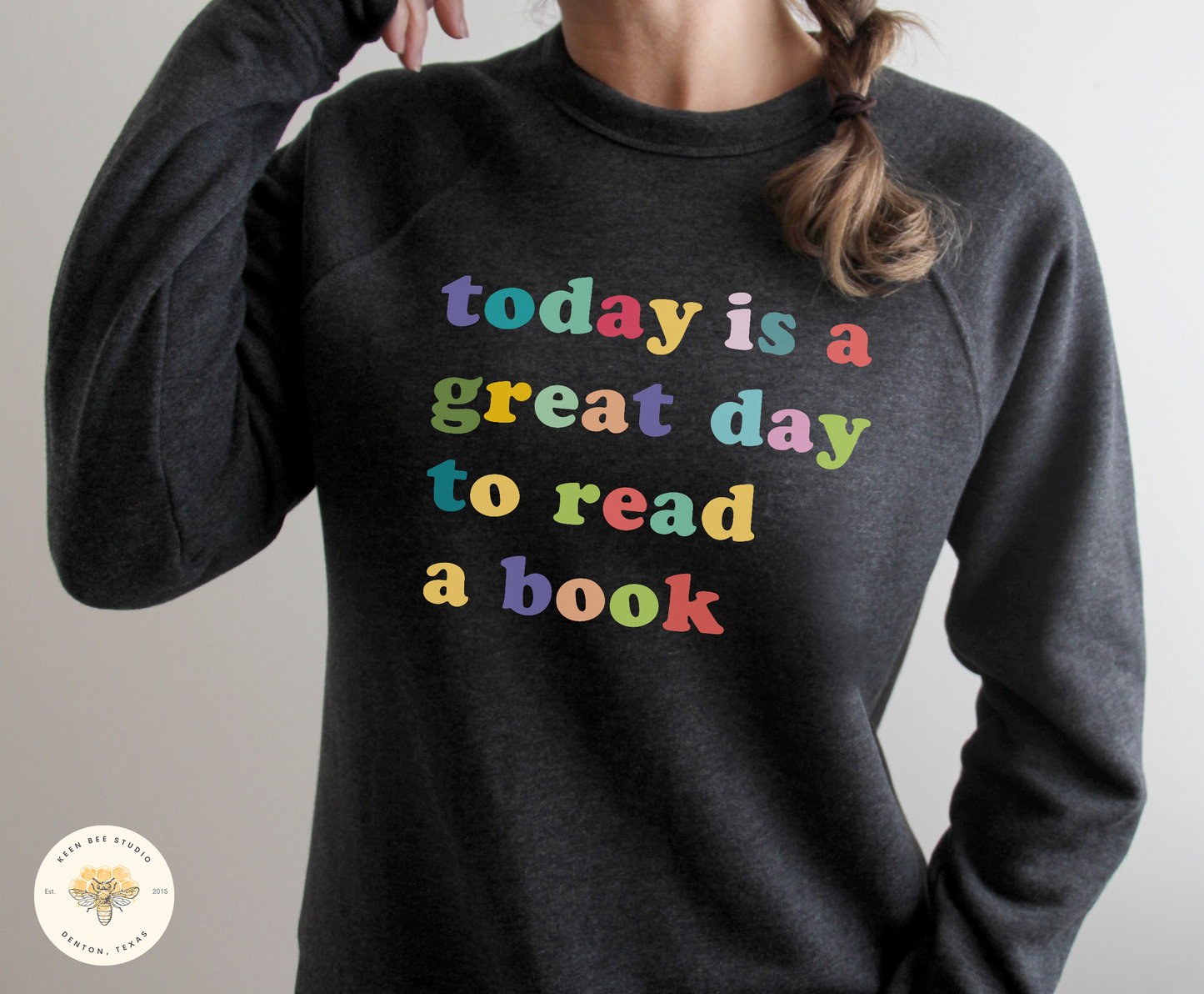A person wearing a gray sweatshirt with the text "Today is a great day to read a book" printed on it.