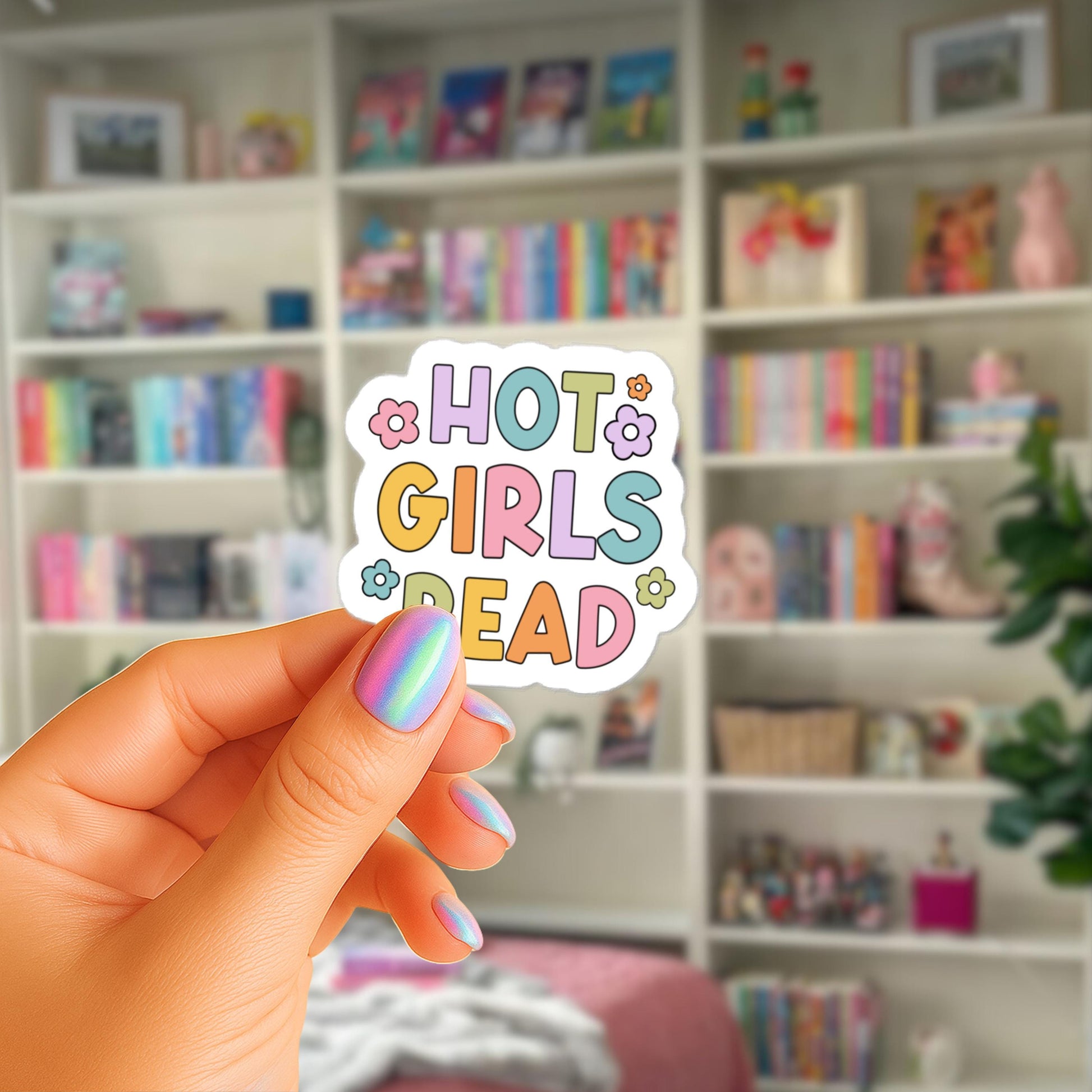 A hand holding a sticker with the text "HOT GIRLS READ" in a colorful, playful font.