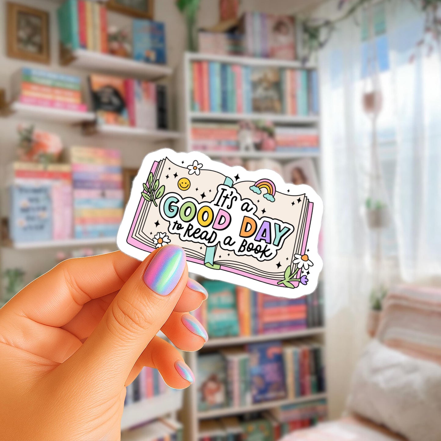 A hand holding a sticker with the text "It's a good day to read a book" against a background of a bookshelf filled with books.