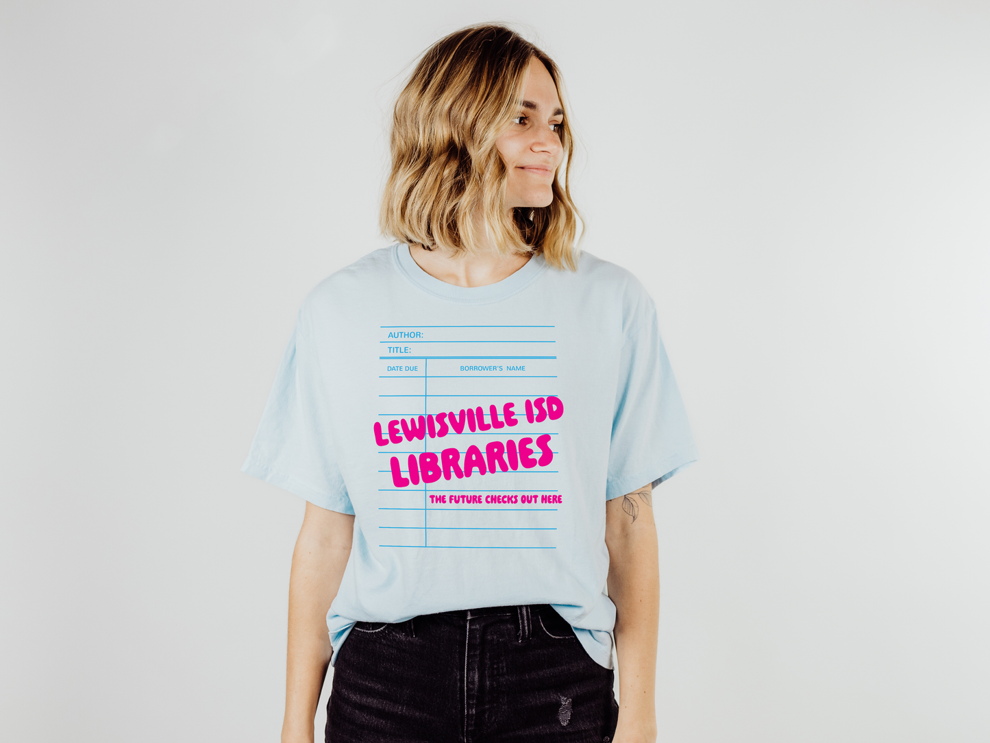 A woman wearing a light blue t-shirt with text printed on it, standing against a plain white background.
