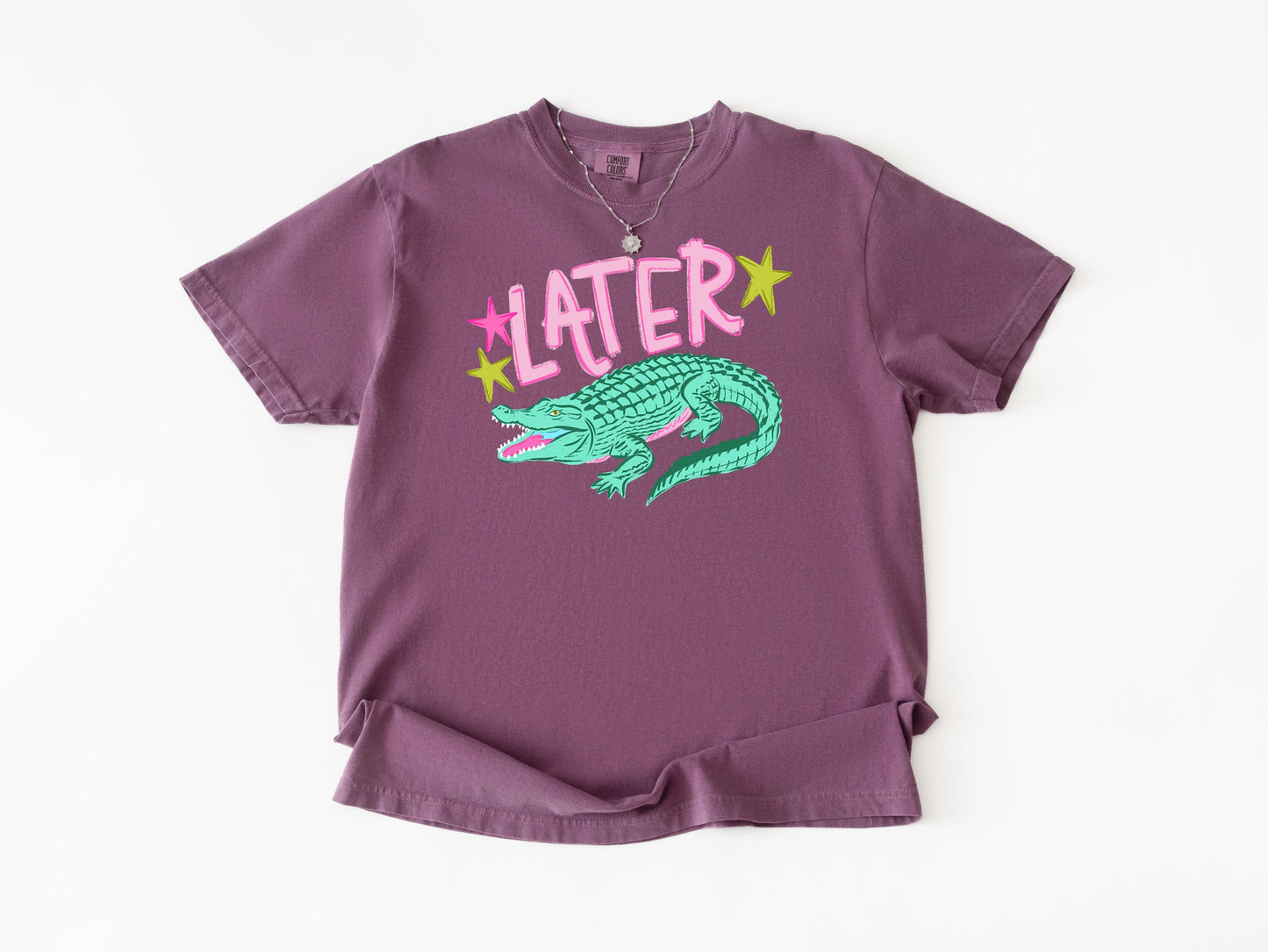 a purple t-shirt with a graphic design of a green alligator and the word "later" written above it.