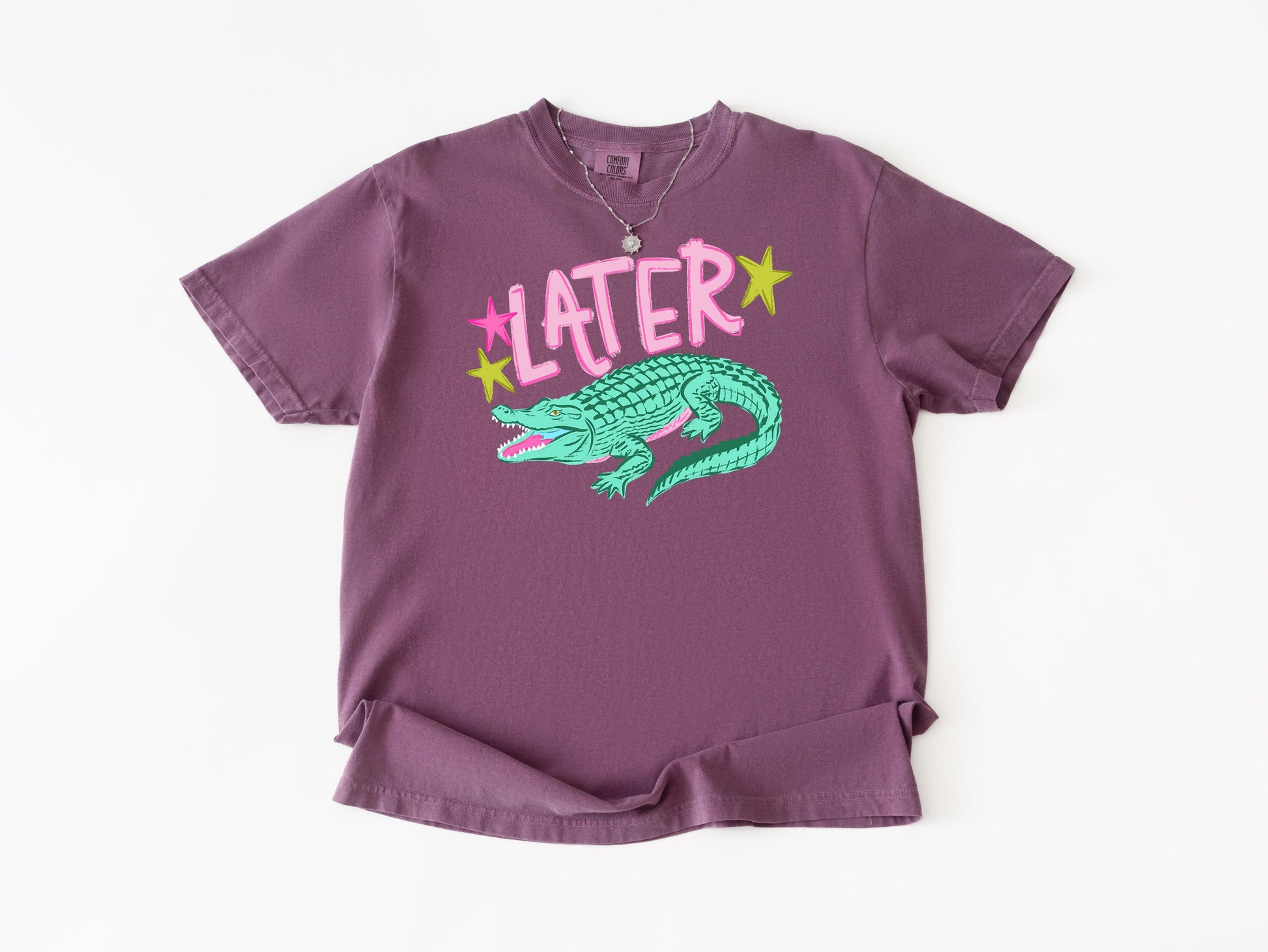 a purple t-shirt with a graphic design of a green alligator and the word "later" written above it.