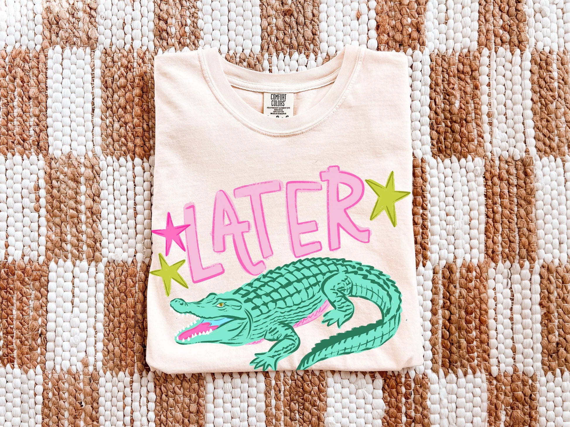 a white t-shirt with a graphic design of a green alligator and pink stars.