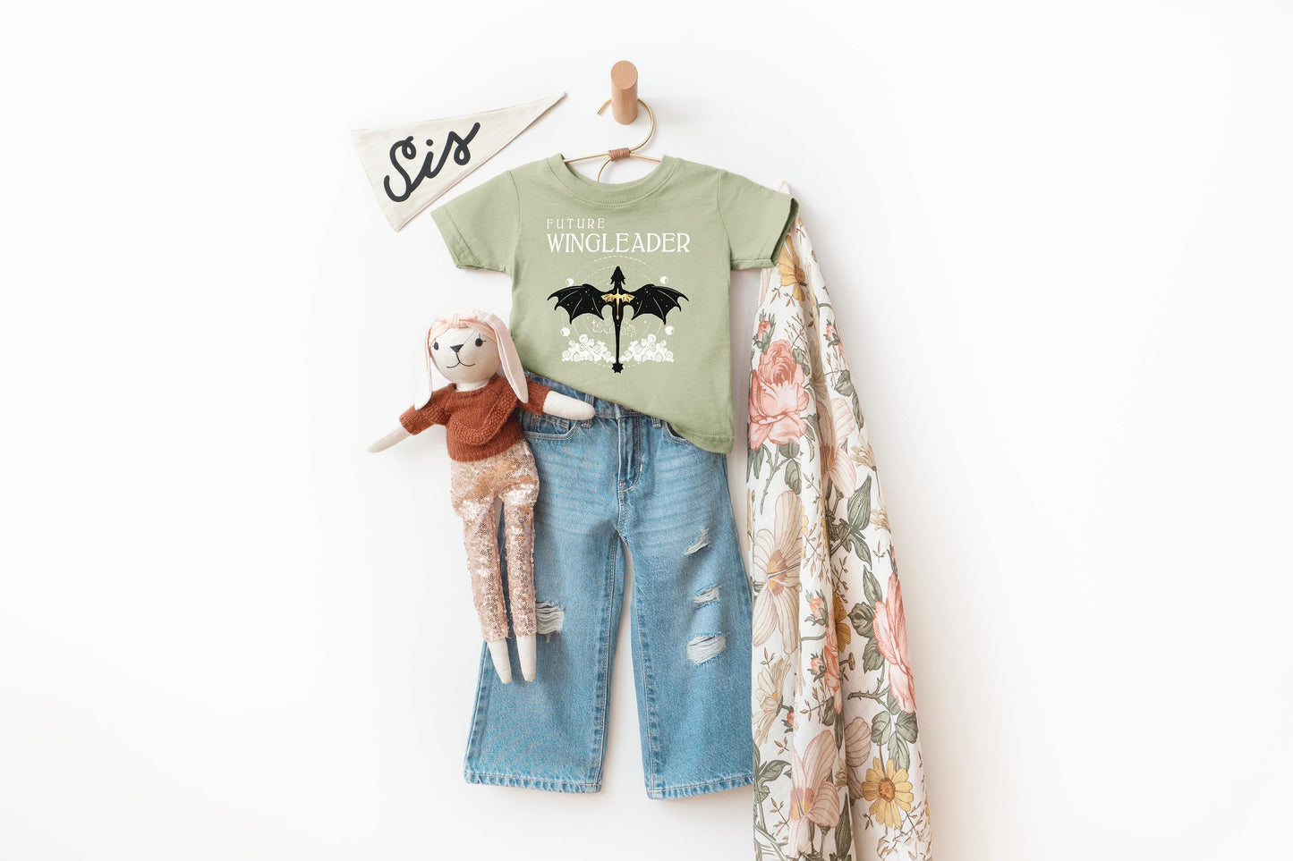 A green t-shirt with a dragon design, a pair of blue jeans, and a stuffed animal rabbit are displayed on a hanger against a white background.