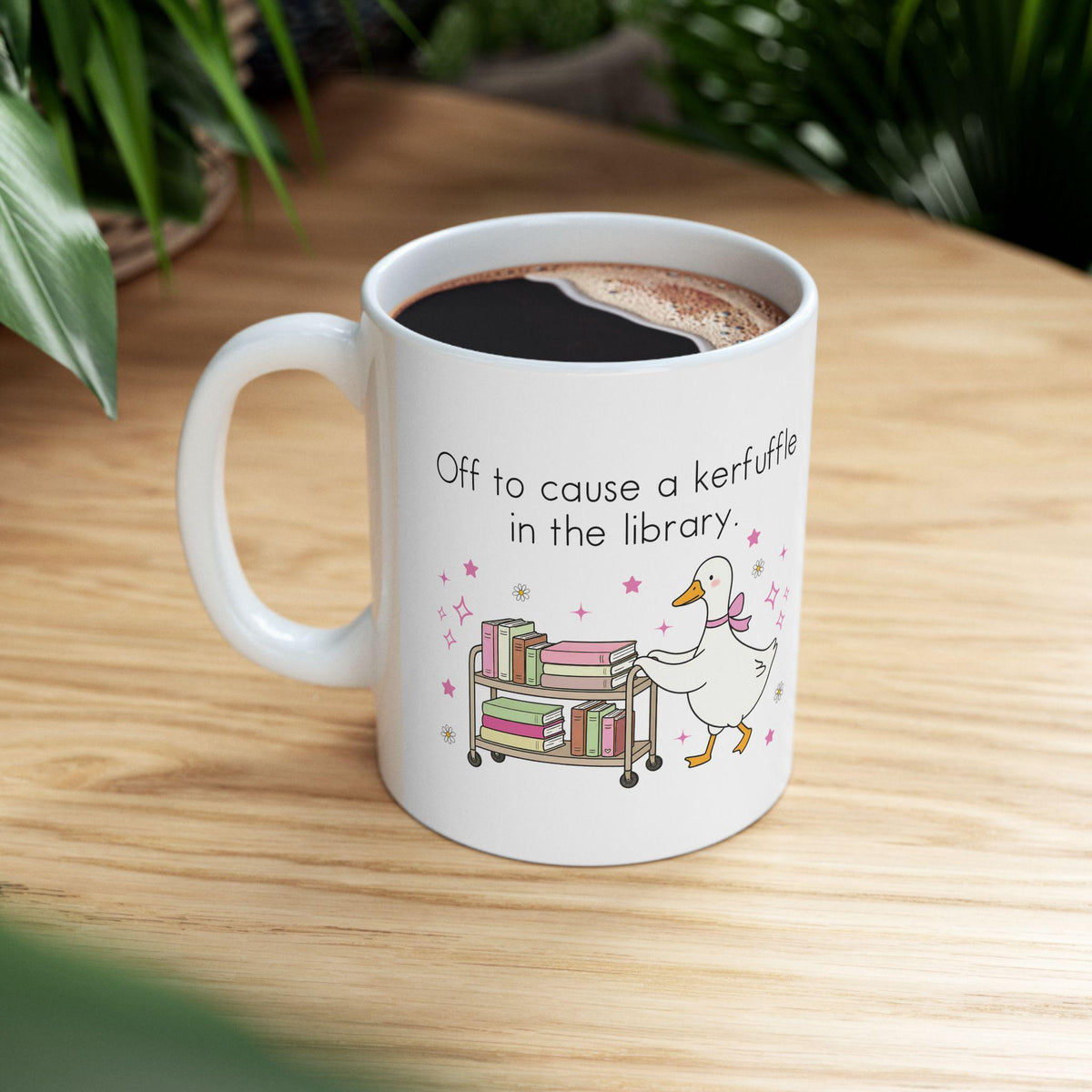 A white mug with a humorous text and an illustration of a duck pushing a cart of books.