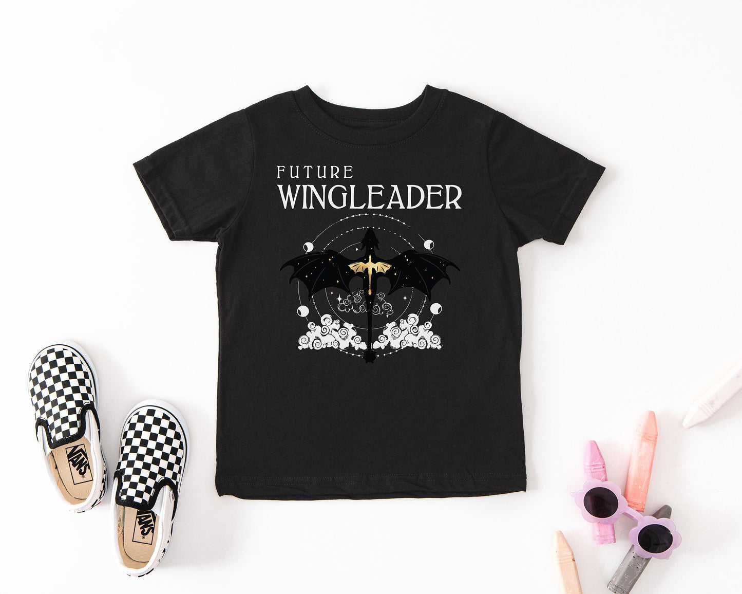 a black t-shirt with a graphic design, a pair of black and white checkered shoes, and some colored pencils.