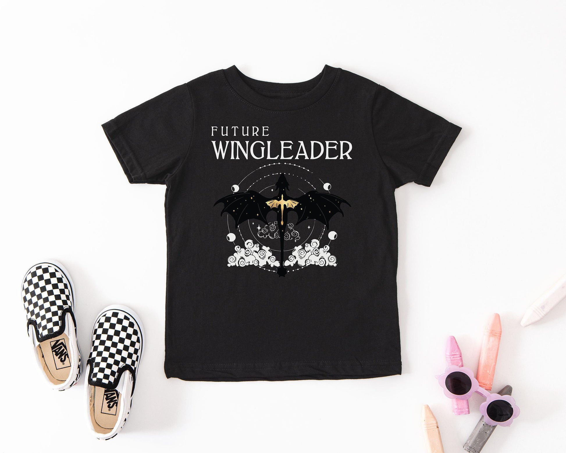 a black t-shirt with a graphic design, a pair of black and white checkered shoes, and some colored pencils.