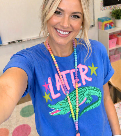 A smiling woman wearing a blue t-shirt with a graphic of a green alligator and colorful beads around her neck.