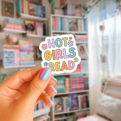 A hand holding a sticker with the text "HOT GIRLS READ" in a colorful, playful font.