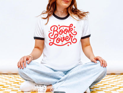 A woman wearing a white t-shirt with red text and jeans is sitting cross-legged on a checkered floor.