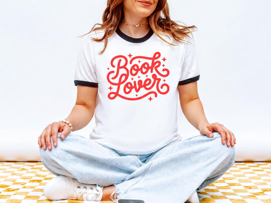 A woman wearing a white t-shirt with red text and jeans is sitting cross-legged on a checkered floor.